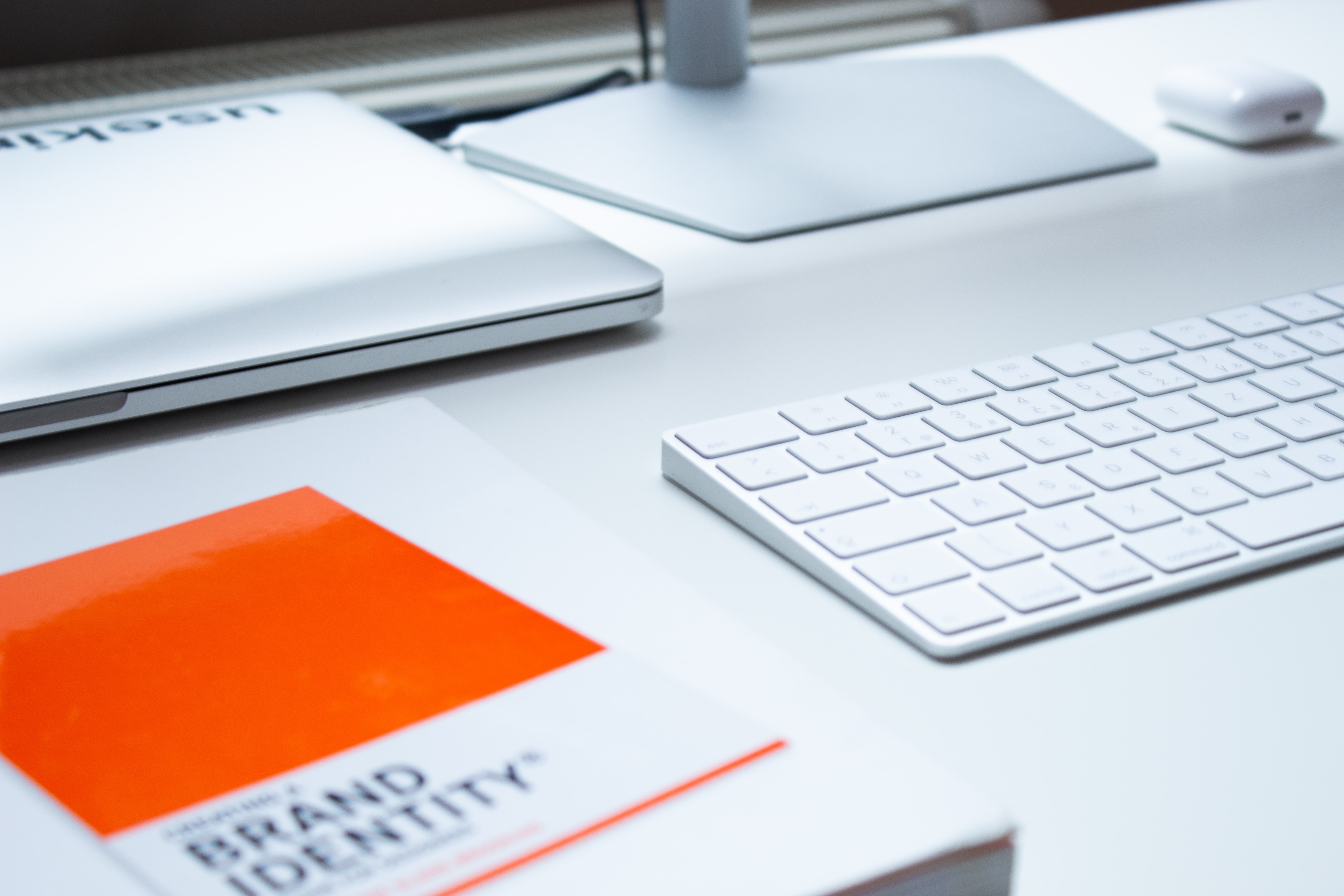 Minimalistic workspace with a brand identity book, a closed laptop, a white keyboard, and a mouse on a clean desk